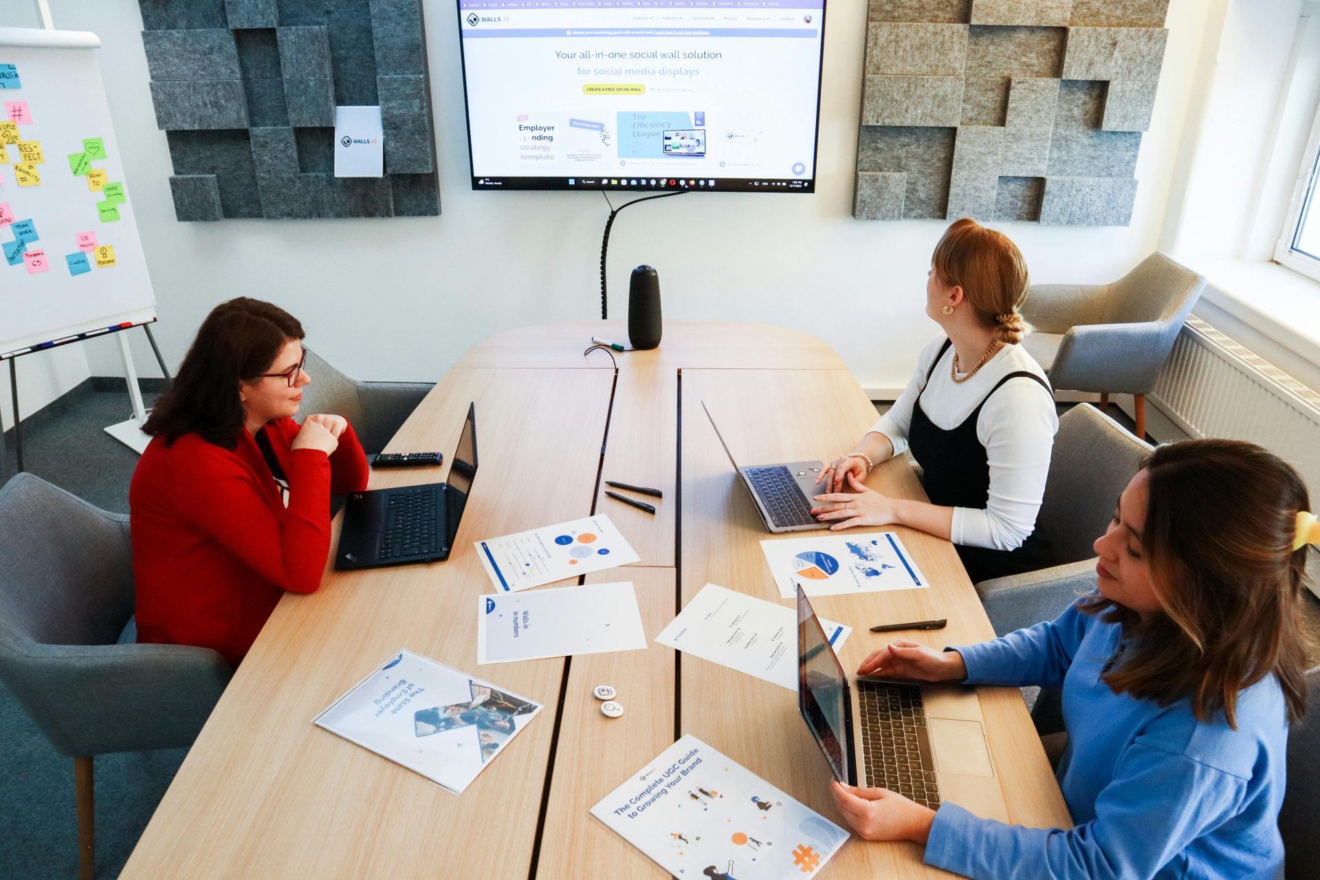 Drei Frauen arbeiten in einem modernen Büro mit Laptops und Präsentationsmaterialien zusammen.